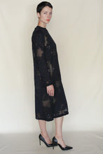Load image into Gallery viewer, A person with short dark hair stands sideways against a beige background, wearing the black Silk Uragiri Crewneck Dress by Lan Jaenicke and black high heels.