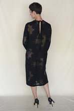 Load image into Gallery viewer, A person with short dark hair faces away, wearing the Silk Uragiri Black Crewneck Dress from Lan Jaenicke featuring sheer, long sleeves and floral patterns, paired with black high heels, set against a light background.