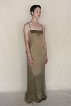 Load image into Gallery viewer, A person with short dark hair stands against a beige background, eyes closed and arms at their sides, wearing the Silk Cord Dress | Gold—an elegant example of handmade San Francisco style.