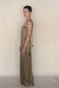 A person with short dark hair wears a sleeveless, floor-length Silk Cord Dress with black spaghetti straps, standing sideways against a plain beige background. They accessorize with gold earrings and a bracelet.