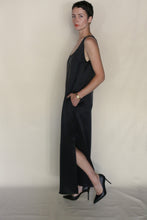Load image into Gallery viewer, A woman with short dark hair wears the sleeveless black Ink Stone Dress, styled with black heels and a gold watch, standing in profile against a beige background with one hand in her pocket.