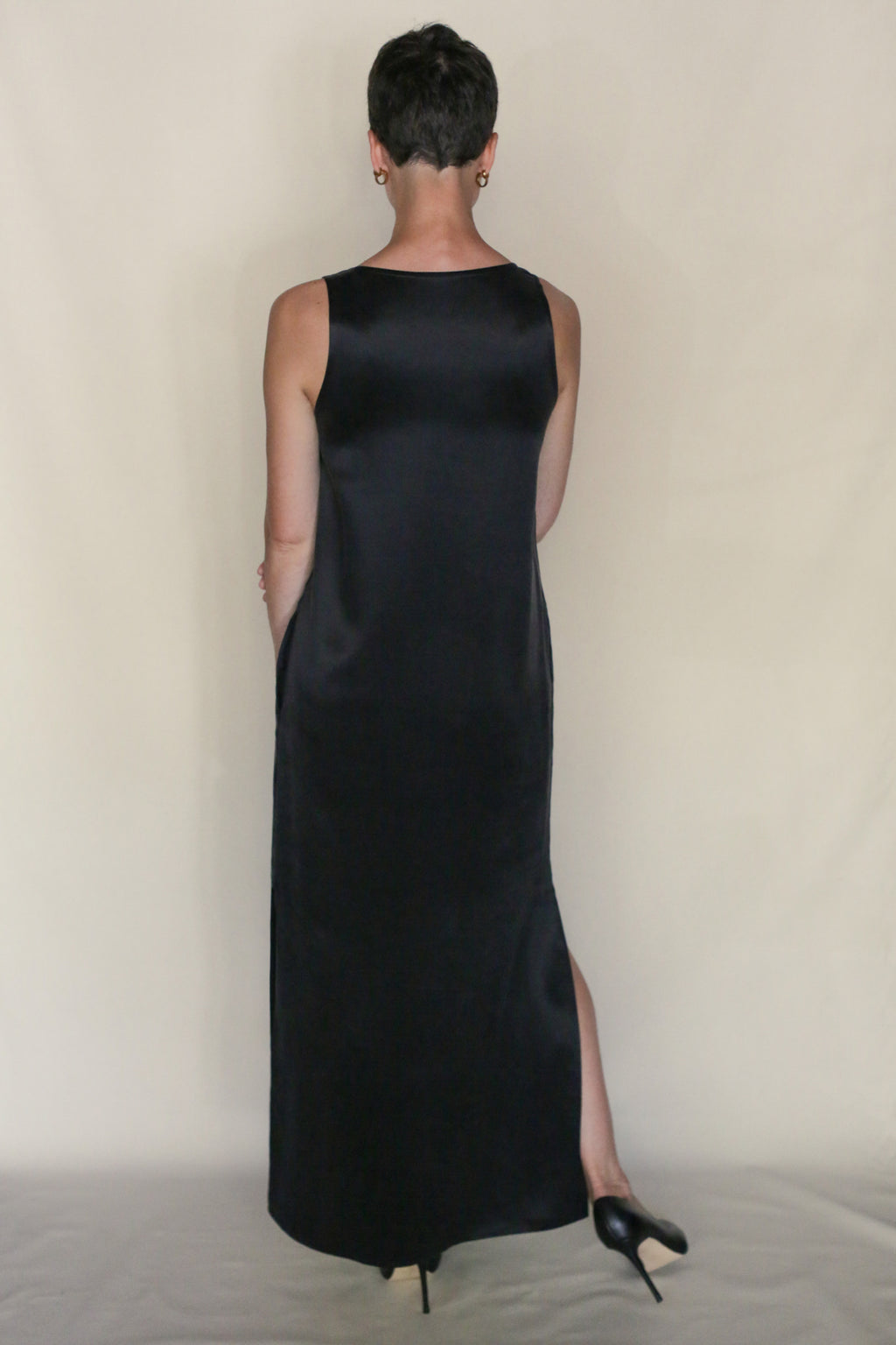 A person with short hair wears the sleeveless, long black Ink Stone Dress, facing away from the camera against a plain light background. The look highlights the elegance of this handmade San Francisco cupro dress.