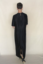 Load image into Gallery viewer, A person with short hair stands facing away from the camera against a plain, light background, wearing the Xiang Yun Silk Earth Mark Crewneck Dress in black and paired with black high heels.