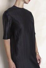 Load image into Gallery viewer, A person in the Xiang Yun Silk Earth Mark Crewneck Dress—a handmade, textured black piece—stands against a light background, wearing a gold wristwatch and turning their head to reveal only part of their face.