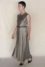 Load image into Gallery viewer, A woman with short hair wears the handmade Bias Dress in Pewter—a sleeveless, ankle-length gray cupro twill dress—styled with a thin black belt, black heels, and a gold watch, walking against a plain light background. Made in San Francisco.