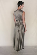 Load image into Gallery viewer, A person with short hair wears the Bias Dress | Pewter— a sleeveless, long, silver bias-cut style—paired with black heels, standing facing away from the camera against a plain light background.