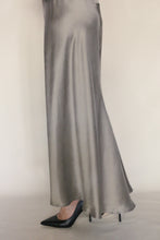 Load image into Gallery viewer, A person stands against a neutral background wearing the Bias Dress in Pewter and black pointed-toe high heels.