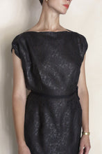 Load image into Gallery viewer, A woman wears the Futo Dress Reversible | Xiang Yun Silk Endless Bloom, a short-sleeved, black patterned dress with a belt and zero-waste design, paired with a gold watch and small gold earrings. She stands against a plain background.