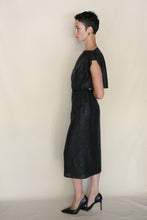Load image into Gallery viewer, A person with short dark hair stands in profile against a plain light background, wearing the black, knee-length Futo Dress Reversible | Xiang Yun Silk Endless Bloom, designed for zero waste. Their hands are behind their back and they wear black heels.