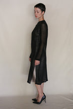 Load image into Gallery viewer, A person with short dark hair stands sideways in a long-sleeved, semi-sheer Crewneck Dress | Linen Leno Black and black heels against a plain light background.