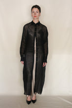 Load image into Gallery viewer, A person with short dark hair wears the Atelier Coat | Linen Lino Black—a sheer black linen coat by Lan Jaenicke—over a light beige outfit and black pointed shoes, standing against a plain, light background. Handmade in San Francisco.