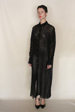 Load image into Gallery viewer, A person with short dark hair models the Atelier Coat | Linen Lino Black—a long, sheer black button-up coat with long sleeves and black pointed shoes—against a plain background for an elegant Atelier Lan Jaenicke look.