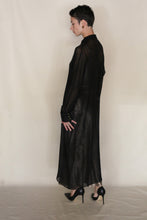 Load image into Gallery viewer, A person with short dark hair in a long, sheer black dress and heels stands sideways against a plain background, layered with the Atelier Coat | Linen Lino Black by Lan Jaenicke, handmade in San Francisco.