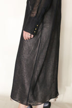 Load image into Gallery viewer, A person wears a sheer black long-sleeved dress with gold cuffs, revealing part of their hand and leg, styled with the Atelier Coat | Linen Lino Black by Lan Jaenicke, handmade in San Francisco, standing against a plain light background.
