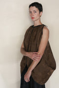 A woman with short dark hair and gold earrings wears the Lingering Fragrance Butterfly—a brown, loose, sleeveless reversible silk top—standing against a neutral background with arms crossed, gazing forward calmly.