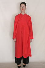Load image into Gallery viewer, Against a plain background, a person with short dark hair and a neutral expression wears the Qipao Dresscoat | Organic Typewriter Vermilion over black pants and shoes. The loose red coat is crafted from organic typewriter cotton.