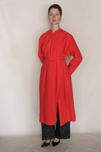 Load image into Gallery viewer, A person stands against a plain background wearing the Qipao Dresscoat | Organic Typewriter Vermilion, featuring a long bright red coat with a slit, paired with black wide-leg pants and pointed-toe shoes—crafted for an elevated San Francisco style.