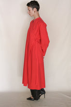 Load image into Gallery viewer, A person with short hair stands sideways in the Qipao Dresscoat | Organic Typewriter Vermilion, tied at the waist, paired with black pants and pointed heels—handmade in San Francisco.