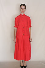 Load image into Gallery viewer, Against a light beige background, a person wears the Work Shirt Crop | Organic Typewriter Cotton Vermillion with rolled sleeves, matched to a red pleated skirt in the same fabric, complemented by black heels.