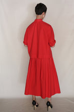 Load image into Gallery viewer, A person with short dark hair wears the Column Wrap Skirt in Organic Typewriter Cotton Vermillion and black heels, facing away from the camera against a neutral background.