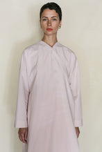 Load image into Gallery viewer, A person with short dark hair stands against a light background, wearing the Qipao Dresscoat | Organic Typewriter Cotton Blush—handmade, long-sleeved, loose fit, and crafted from organic typewriter cotton in pale pink.