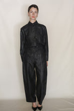 Load image into Gallery viewer, A woman with short hair stands against a plain light background, wearing the black Studio Shirt | Xiang Yun Silk Earth Mark with matching high-waisted, wide-leg pants and black shoes, looking directly at the camera.