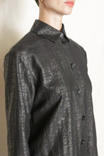Load image into Gallery viewer, A person wearing the Studio Shirt | Xiang Yun Silk Earth Mark in textured black, with a collar, stands against a light background. Only the upper body and part of the face are visible.