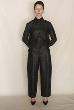 Load image into Gallery viewer, A person with short dark hair stands against a light background, wearing a black, textured Xiang Yun Silk button-up shirt and Barrel Leg Trousers | Xiang Yun Silk Earth Mark for a modern silhouette, paired with black pointed-toe shoes.