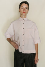 Load image into Gallery viewer, A person with short hair stands against a plain light background, wearing the Work Shirt Crop in blush organic typewriter cotton—handmade in San Francisco—paired with black pants and a neutral expression.