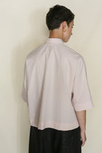 Load image into Gallery viewer, A person with short brown hair, wearing the Work Shirt Crop | Organic Typewriter Cotton Blush and black pants, stands facing away from the camera against a plain light background.