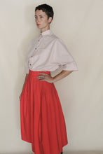 Load image into Gallery viewer, A person with short dark hair poses against a plain background, wearing the Work Shirt Crop in Organic Typewriter Cotton Blush, tucked into a high-waisted, bright red A-line skirt.