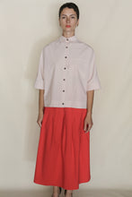 Load image into Gallery viewer, Against a plain background, a person wears the Work Shirt Crop in Organic Typewriter Cotton Blush, styled with a high-waisted, bright red pleated midi skirt—both handmade with care in San Francisco.