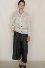 Load image into Gallery viewer, A person with short hair wears the Sumi Top | Silk Mesh and wide-leg black pants, standing against a plain beige background with one hand in their pocket—a perfect lightweight, handmade San Francisco cover-up.