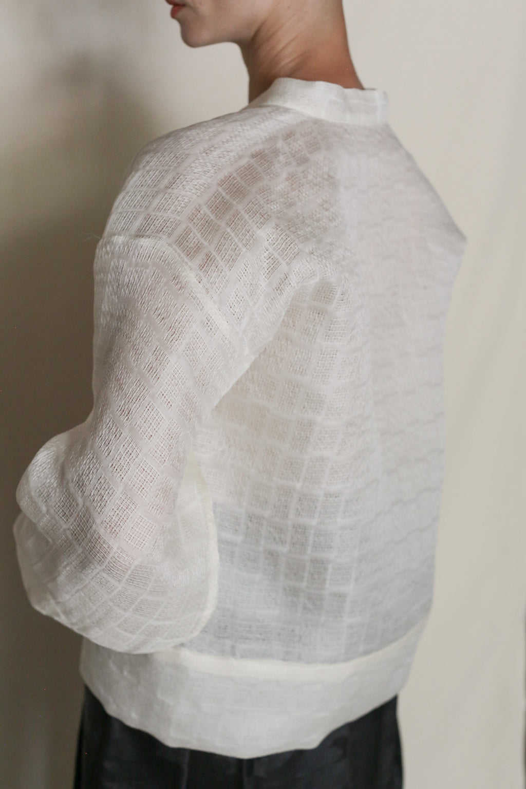 A person wears the Silk Mesh Sumi Top, a sheer white silk mesh with a grid pattern, loose sleeves, and a boxy fit, photographed from the side and back against a neutral background.