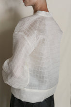 Load image into Gallery viewer, A person models the Sumi Top | Silk Mesh—a semi-sheer white silk mesh top with a grid texture and loose sleeves—shown from the side and back against a neutral background.