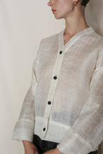 Load image into Gallery viewer, A person wearing the Sumi Top | Silk Mesh, a sheer white handmade piece from San Francisco with black buttons and gold hoop earrings, shown shoulders up and slightly turned against a plain light background.