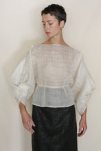 Load image into Gallery viewer, A person with short dark hair wears the Origami | Silk Mesh sheer white top with wide sleeves and a black skirt, standing against a plain light background and looking slightly to the side.