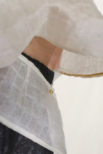 Load image into Gallery viewer, Close-up of a person in the Origami | Silk Mesh top, showcasing its textured white silk mesh, gold detailing, zero-waste design accents, and a small gold button. Paired with a black skirt featuring an elastic waistband.