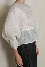 Load image into Gallery viewer, A person wears the Origami | Silk Mesh Top—sheer, textured, white with wide sleeves and a fitted waist—paired with a black skirt while standing against a plain background.