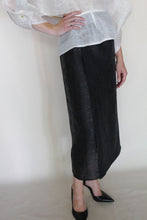 Load image into Gallery viewer, A person stands against a neutral background wearing a sheer white blouse, black pointed-toe heels, and the Reversible Futo Skirt in Xiang Yun Silk Endless Bloom. The skirt is high-waisted and midi-length; the face is not visible.