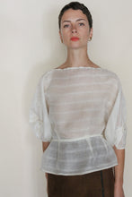 Load image into Gallery viewer, A person with short hair wears the Origami | Silk Double Cloth Woven Veil, a sheer white, textured blouse with wide sleeves inspired by zero-waste design, paired with gold hoop earrings, standing against a plain light background and looking at the camera.