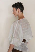 Load image into Gallery viewer, A person with short dark hair wears the Origami | Silk Double Cloth Woven Veil top with wide sleeves and gold buttons, standing sideways against a plain light background.