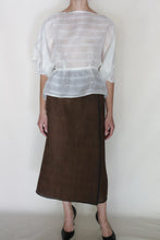Load image into Gallery viewer, A person faces forward in a sheer white blouse with three-quarter sleeves, the Reversible Futo Skirt | Xiang Yun Silk Endless Bloom in brown, and black pointed-toe shoes. The background is plain and light-colored.