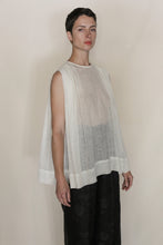 Load image into Gallery viewer, A person with short dark hair wears the Shoulder Pleat Top | Linen Leno Ivory, a sleeveless, loose, sheer white top, over black wide-leg pants against a plain light background, looking at the camera with a neutral expression.