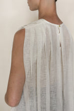 Load image into Gallery viewer, A person wears the Shoulder Pleat Top | Linen Leno Ivory, a sheer white linen blouse with pleated shoulders and a small back button, crafted in handmade San Francisco style. The lightweight, slightly transparent fabric reveals the shoulder outline.