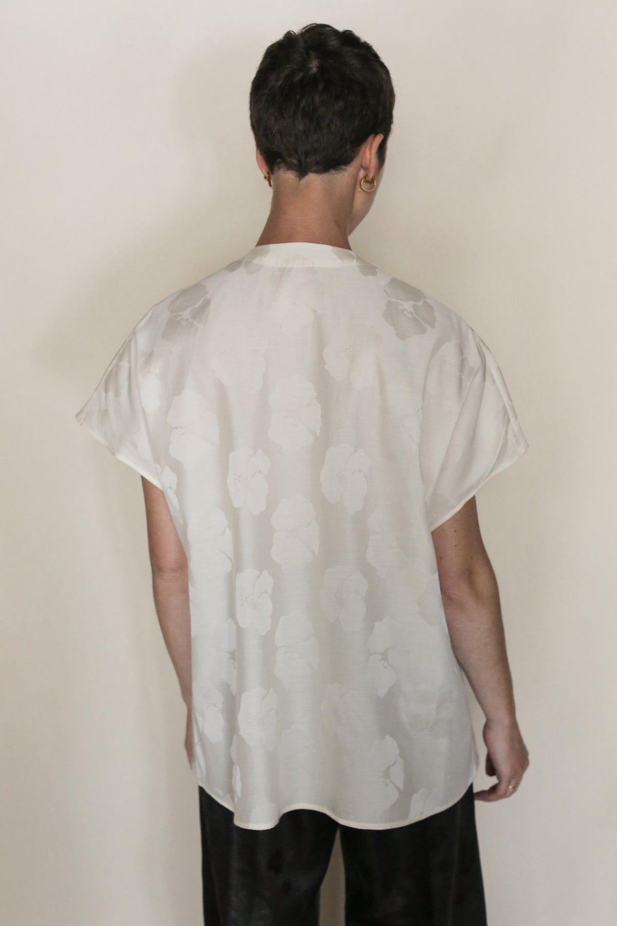 A person with short dark hair faces away from the camera, wearing the Hidden Peony Qipao Vest and black pants, set against a plain light background.