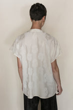 Load image into Gallery viewer, Person with short dark hair, seen from behind, wears the Qipao Vest Hidden Peony Undyed—a loose jacquard blouse with a subtle floral pattern—and black pants, standing against a plain light background.