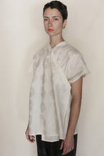 Load image into Gallery viewer, A person with short dark hair and gold hoop earrings stands against a plain background, wearing the Qipao Vest Hidden Peony Undyed and black pants, with a neutral expression.