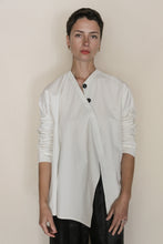 Load image into Gallery viewer, A person with short dark hair wears the Qipao Blouse | Cotton Omizarashi Undyed, a loose, long-sleeved white top, standing against a plain light background and looking directly at the camera with a neutral expression. Handmade in San Francisco.