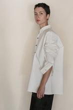 Load image into Gallery viewer, A person with short dark hair models the Men's Shirt | Cotton Omizarashi Undyed, sleeves rolled up, paired with black pants, standing sideways against a plain beige background.